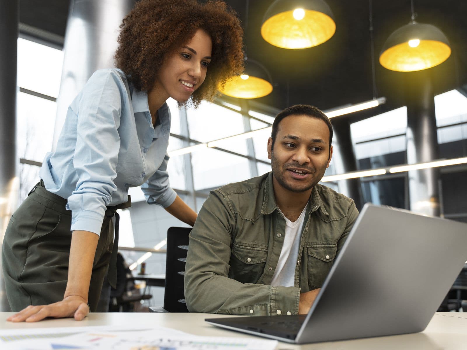 A small agency team at work: a woman leans over to talk through something on a colleague's laptop.