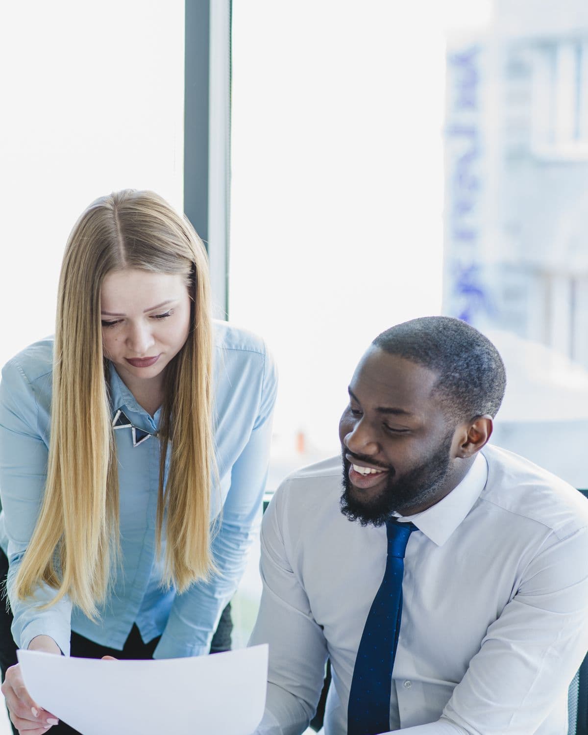 Two colleagues in a bright office going through a printed report together.