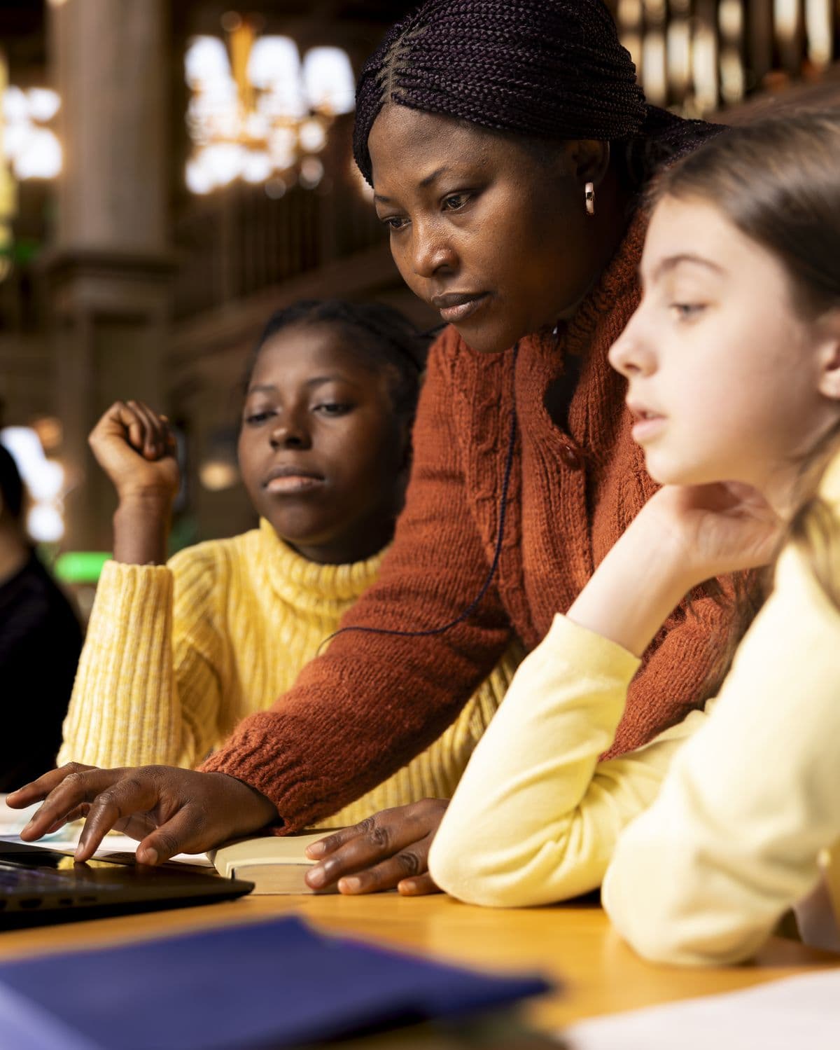 A teacher working through a lesson with two students in a school library.
